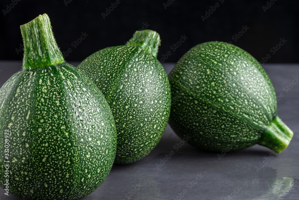 Close-up of three round zucchini on dark gray background, with selective focus and black background, horizontal Close-up of three round zucchini on dark gray background, with selective focus and black background, horizontal