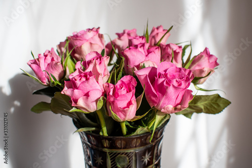 Bouquet of fresh delicate light pink roses and blurred green leaves in a vase in a sunny summer day, beautiful indoor floral background photographed with soft focus