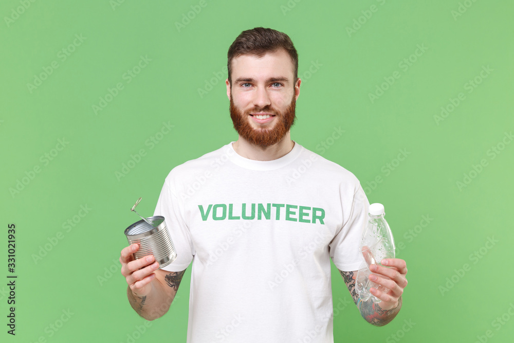 Smiling young bearded man in white volunteer t-shirt isolated on pastel green background. Voluntary free work assistance help charity grace teamwork concept. Hold trash empty plastic bottle, tincan. Smiling young bearded man in white volunteer t-shirt isolated on pastel green background. Voluntary free work assistance help charity grace teamwork concept. Hold trash empty plastic bottle, tincan.