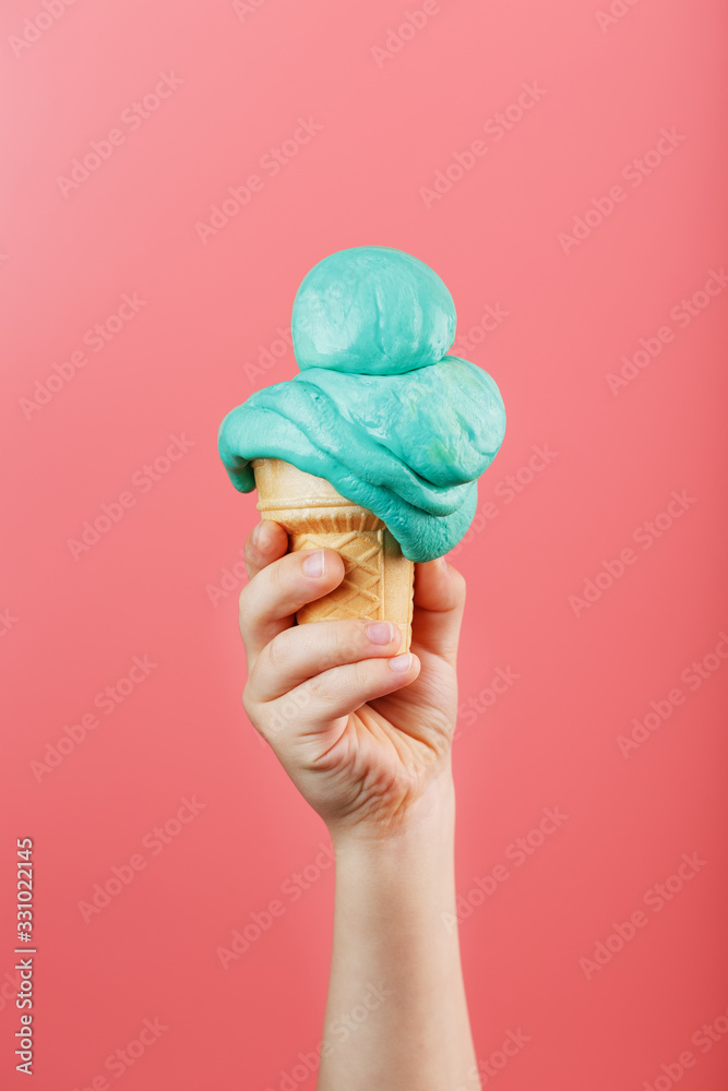 Ice cream in a child's hand melts on a pink background. The waffle cone with blue ice cream melts.