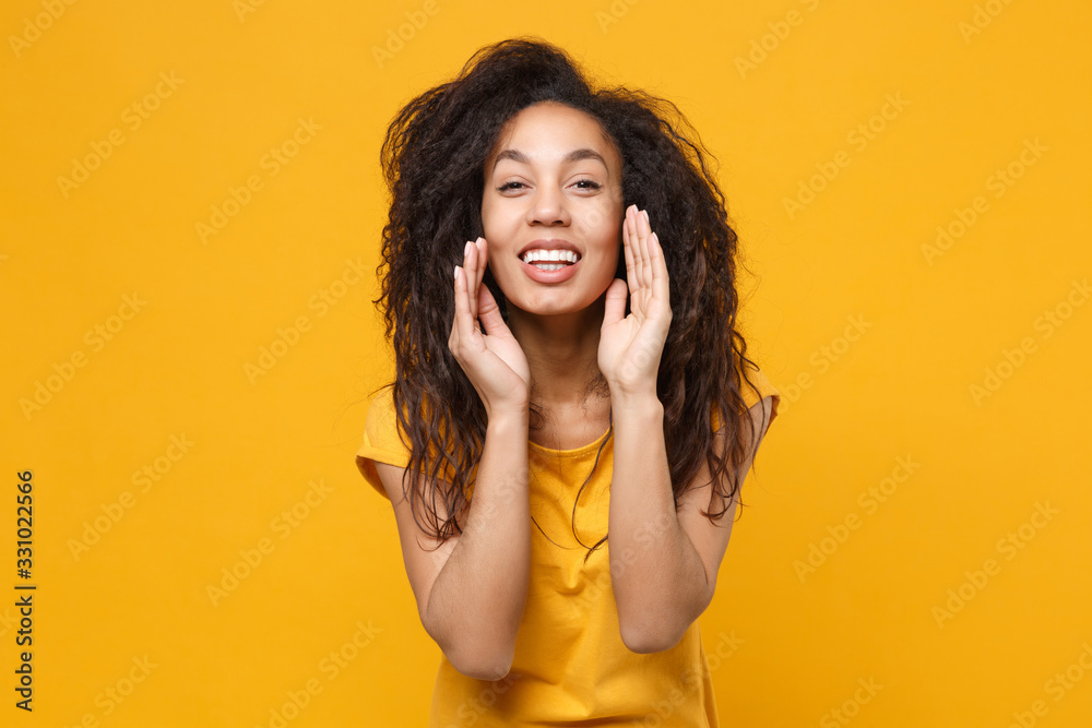 Cheerful young african american woman girl casual t-shirt posing isolated on yellow orange background in studio. People lifestyle concept. Mock up copy space. Screaming with hands gesture near mouth. Cheerful young african american woman girl casual t-shirt posing isolated on yellow orange background in studio. People lifestyle concept. Mock up copy space. Screaming with hands gesture near mouth.