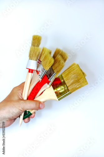 Fototapeta Naklejka Na Ścianę i Meble -  Artist hand with brush for painting. Hand holding a thick brushes isolated on a light background. A new miscellaneous paint brushes with hand in closeup