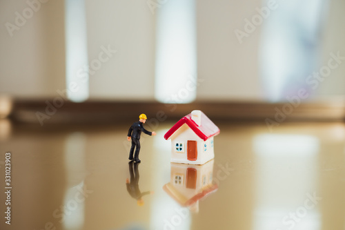 Miniature people, builder wearing black uniform standing with mini house using as property renovation concept © jaturonoofer