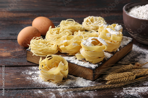 Concept of Italian cuisine. Dry pasta fettuccine and capellini with bowl with flour  eggs and wheat ears on an old wooden background. Background image  copy space