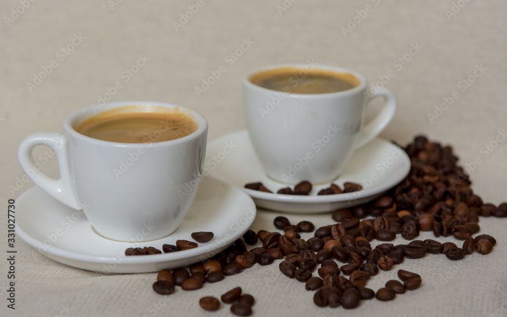 Two cups of fresh espresso with coffee beans. Sprinkled coffee beans. Morning coffee concept Two cups of fresh espresso with coffee beans. Sprinkled coffee beans. Morning coffee concept