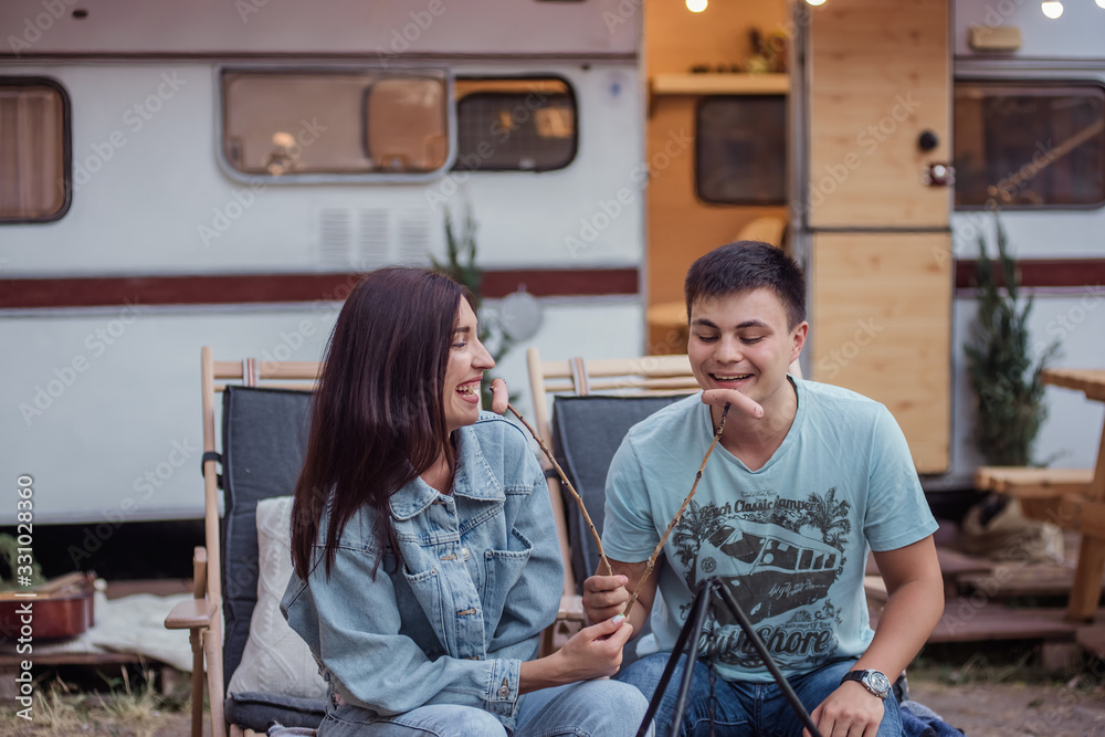 Fototapeta premium A young couple on a honeymoon trip on a trailer. Young husband and wife have fun and grill sausages at the stake.