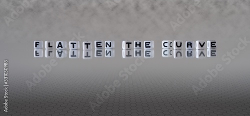 flatten the curve concept represented by black and white letter cubes on a grey horizon background stretching to infinity photo