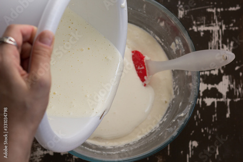 Top view of woman hand pouring whisked eggs into swollen semolina batter as ingredient for baking mannik caressole on the brown background photo