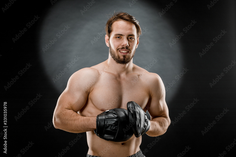 The boxer is a fighter, looking angrily at the camera. Young Caucasian male fitness model isolated on black background