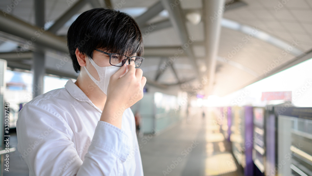 Asian man wearing face mask at skytrain station or urban train platform. Wuhan coronavirus (COVID-19) outbreak prevention in public transportation. Health awareness for PM2.5 air pollution protection. Asian man wearing face mask at skytrain station or urban train platform. Wuhan coronavirus (COVID-19) outbreak prevention in public transportation. Health awareness for PM2.5 air pollution protection.