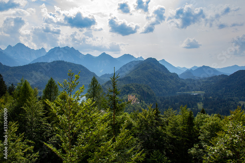 The Bavarian landscape with high forest covered mountains and castles are visible under a cloudy summer sky in Hohenschwangau, Germany