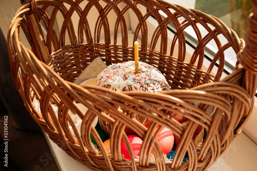 Easter straw basket decorated with a festive napkin with Easter cake and bright decorated eggs and a lit church candle. Peaceful mood. photo