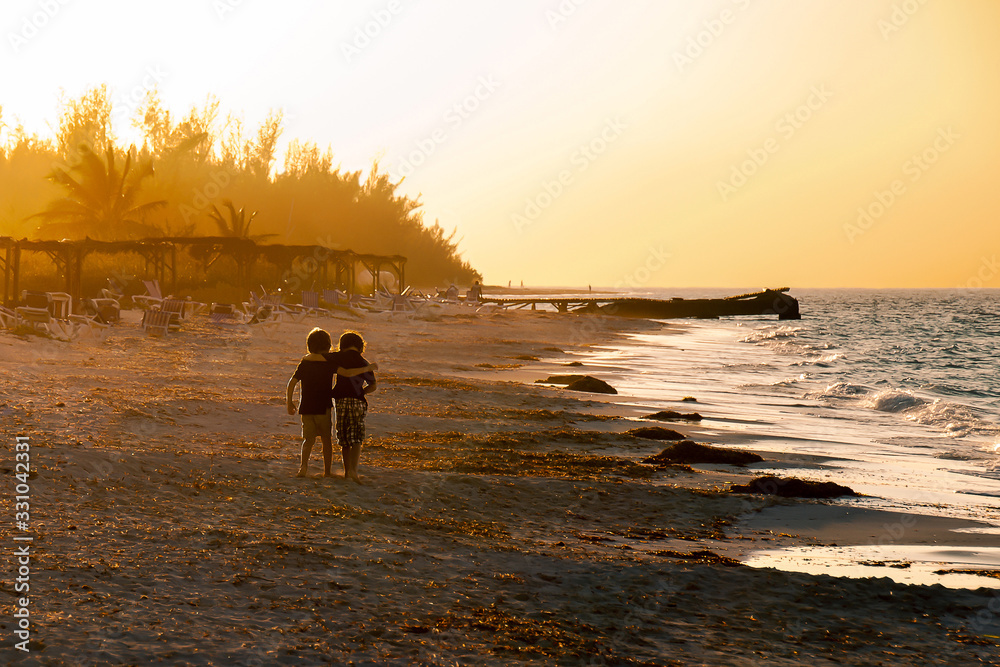 Dos amigos andando hacia el sol al atardecer en la playa Dos amigos andando hacia el sol al atardecer en la playa
