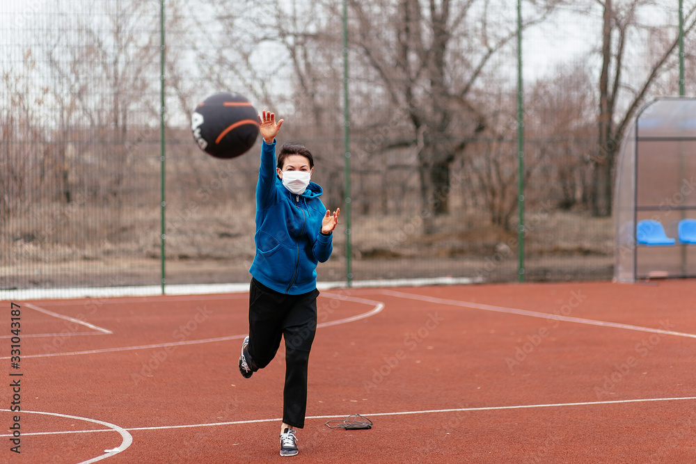 A young woman is playing sports on a sports field in a mask. Protection from coronavirus infection with a medical mask.