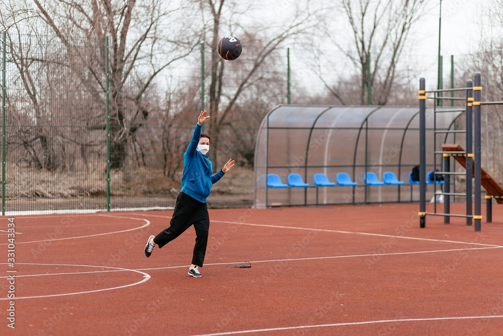 A young woman is playing sports on a sports field in a mask. Protection from coronavirus infection with a medical mask.