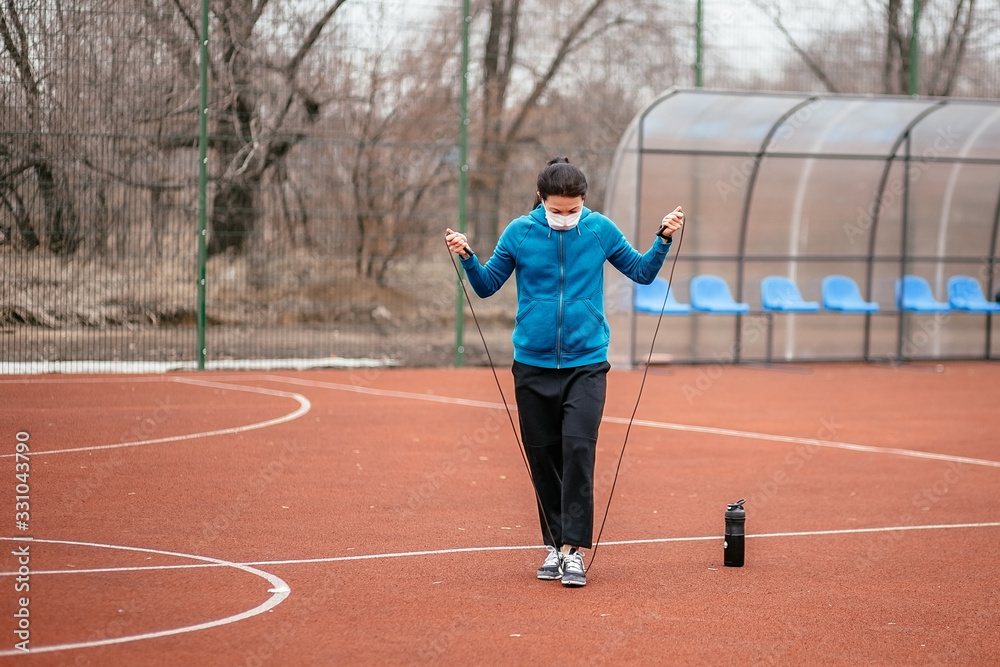 A young woman is engaged in jumping rope in a medical mask. Protection from coronavirus infection with a medical mask.