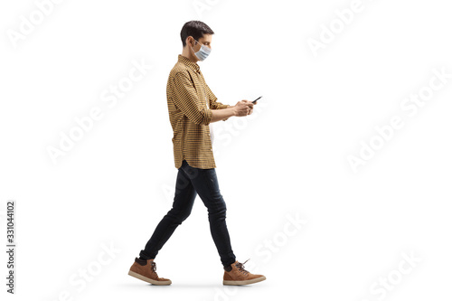 Young man with a medical face mask walking and typing on a mobile phone