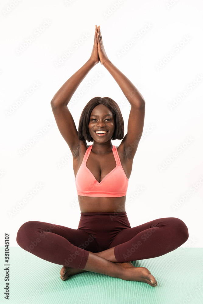 Young happy beautiful african woman during fitness time and exercising, doing yoga while sitting on a blue yoga mat Young happy beautiful african woman during fitness time and exercising, doing yoga while sitting on a blue yoga mat