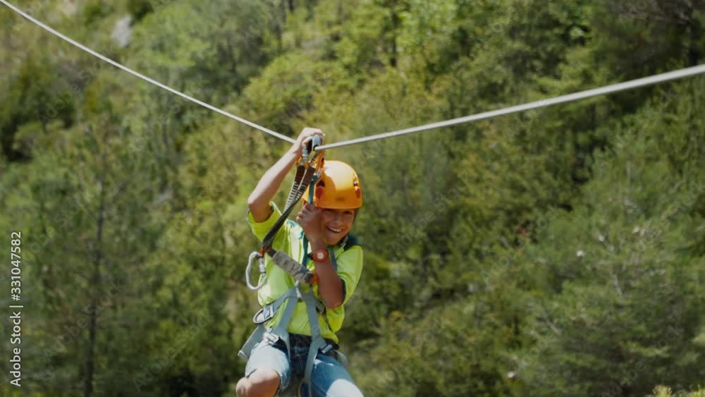 Zip line in mountains, a cable between rocks. Moving with zipline at via ferrata. Small boy use zip line path after hiking to quickly move down to the next mountain. He is happy and exited.