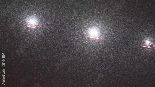 Snowflakes falling from the sky at night, low angle view. Night lights at the background.