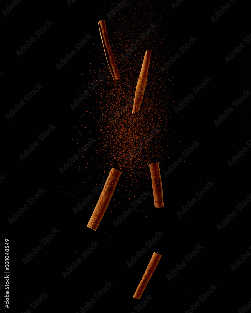 Obraz premium cinnamon sticks and powder falling on a black background. Food explosion, flight levitation. Creative concept