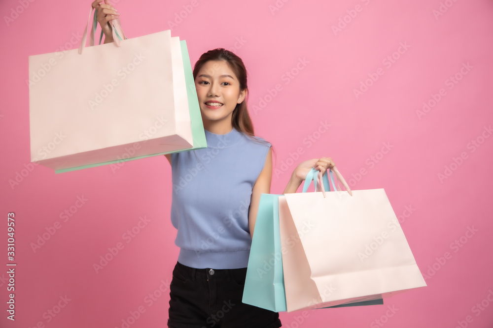 Asian pretty young woman sitting on pink pastel background. She smiling and happy .She hold shopping bags. she nice-looking lovely attractive shine . Asian pretty young woman sitting on pink pastel background. She smiling and happy .She hold shopping bags. she nice-looking lovely attractive shine .
