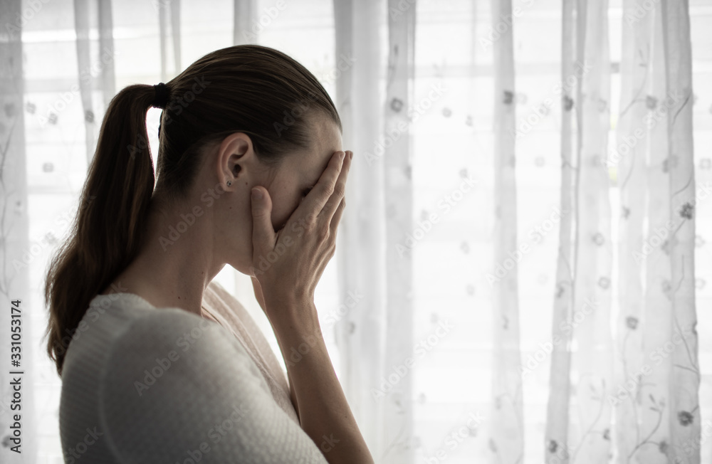 Sad woman and home next to window with hand over face crying. Sad woman and home next to window with hand over face crying.