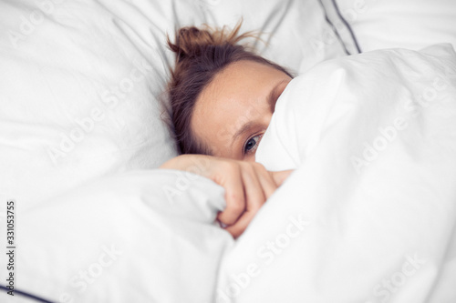 Frau unter weisser Bettdecke wach photo
