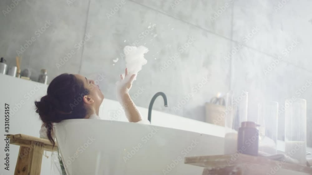 Close up cheerful woman blowing foam in light bathroo imn slow motion.