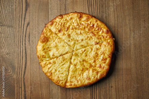 Close up view on tasty traditional Khachapuri - closed baked pie stuffed with melted salt cheese (suluguni) or meat on wooden tray. Traditional georgian food