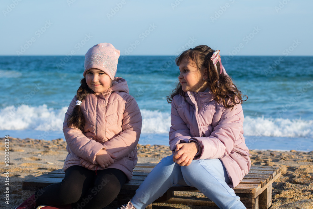 two little caucasian girls in jackets happy to be together on the beach
