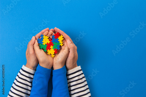 World autism awareness day concept. Adult and child hands holding puzzle heart on light blue background photo