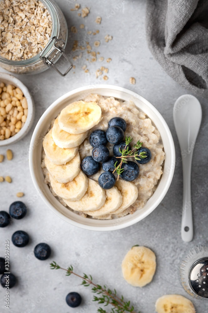 oatmeal with blueberries and banana in a white bowl on a light background. Top view. Breakfast oatmeal with blueberries and banana in a white bowl on a light background. Top view. Breakfast