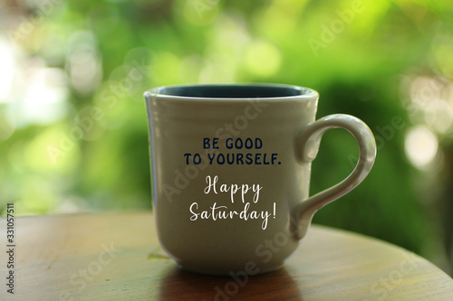 Inspirational quote - Be good to yourself. Happy Saturday concept. With inspiration words on a white cup of hot morning tea or coffee. Blurred green bokeh background. photo