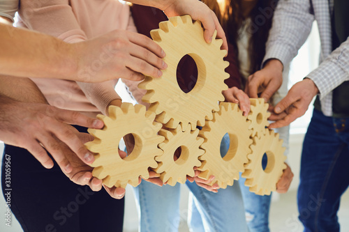 Hands of people hold wooden gears indoors.