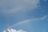 Bright multi-colored rainbow in the blue cloudy sky