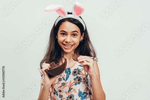 Wall Mural Sweet little girl wearing bunny ears eating chocolate Easter egg