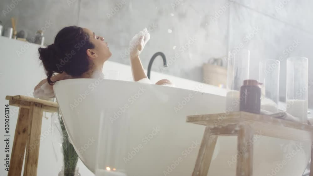 Close up sensual woman blowing foam. Smiling girl having fun with foam in bath.
