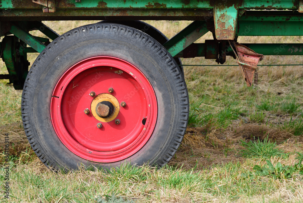 Detail of an old agricultural vehicle, with a red old wheel and tires, on a meadow Detail of an old agricultural vehicle, with a red old wheel and tires, on a meadow
