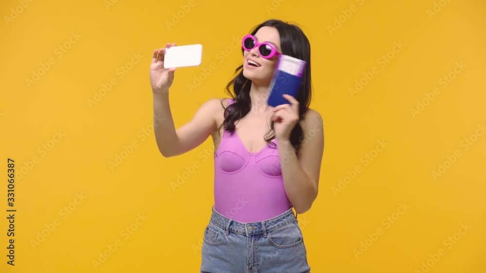 Woman taking selfie with passport and air ticket isolated on yellow Woman taking selfie with passport and air ticket isolated on yellow