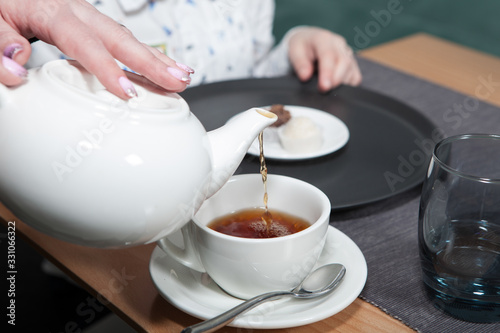 Family Tea Party. Black tea is poured into a tea cup from a white teapot. Close-up