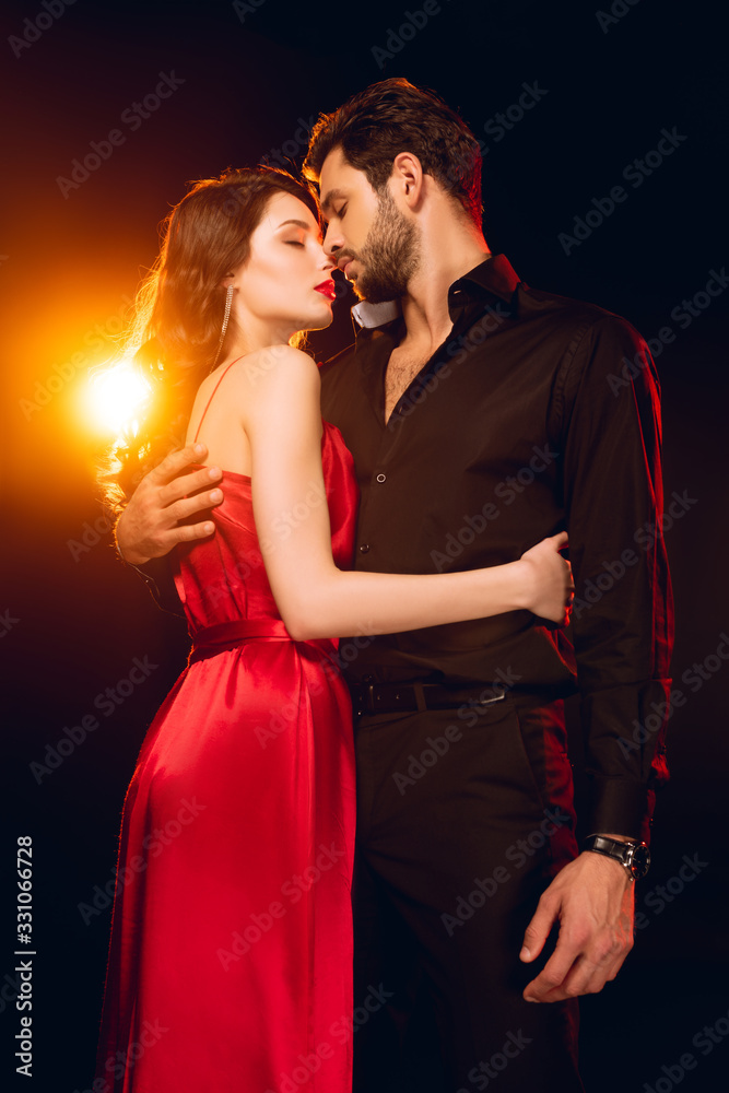 Side view of elegant girl embracing handsome boyfriend on black background with lighting Side view of elegant girl embracing handsome boyfriend on black background with lighting