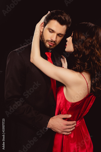 Elegant girl in red dress hugging handsome boyfriend isolated on black