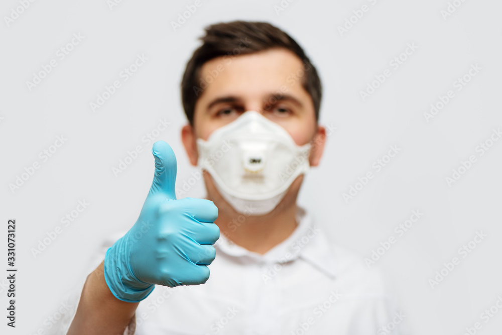 Portrait of doctor in medical uniform with a protective face mask and a gloved hand giving thumbs up. Portrait of doctor in medical uniform with a protective face mask and a gloved hand giving thumbs up.