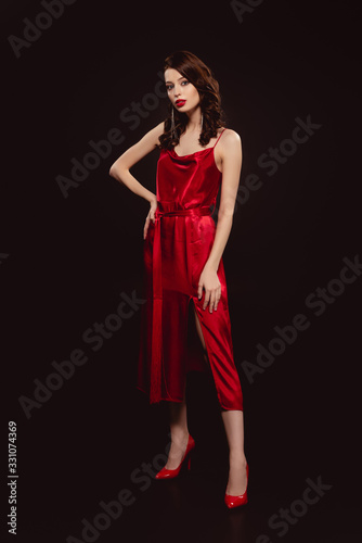 Full length of beautiful woman in red dress looking at camera isolated on black