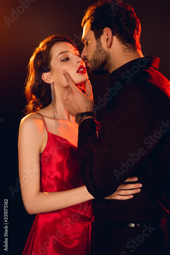Handsome man kissing elegant girlfriend with red lips isolated on black