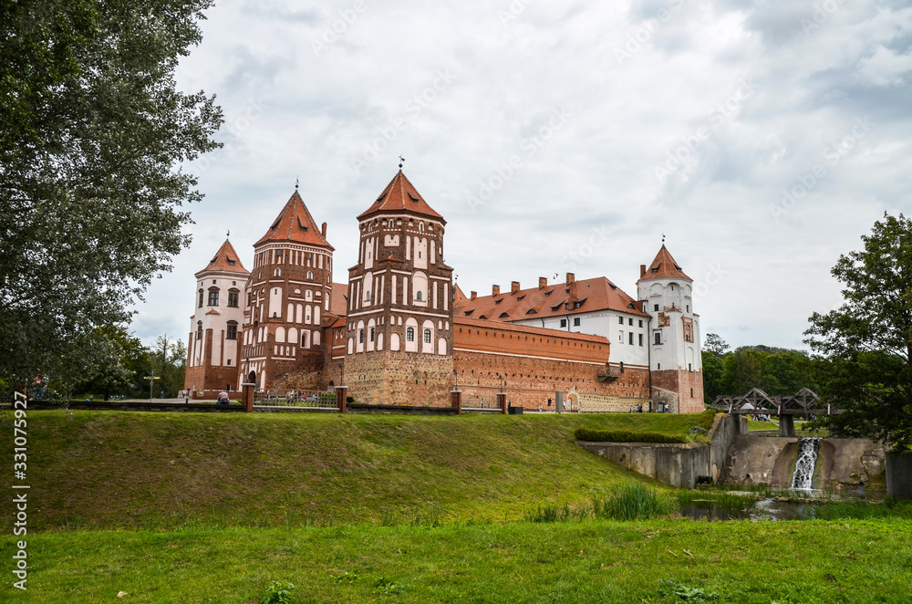 Medieval castle Radzivillov in the settlement of Mir of the Grodno region, Belarus. The fine stone castle and the bridge, Green trees and grass at cloudy day.