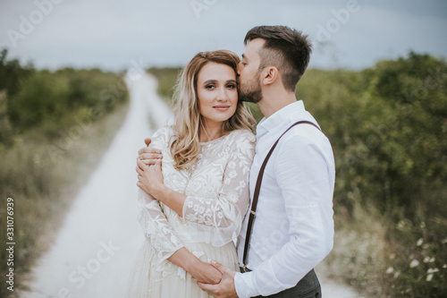 Smiling bride and groom spending time together. Posing on the mountain hills background. Dressed in white dress beautiful blonde caucasian bride and handsome groom. Hugs, kissess and enjoy the company