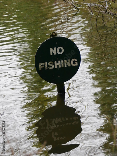 Circular no fishing sign with white letters on dark background on post in water