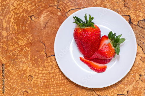 Strawberries on a white saucer. Wooden background, view from the top. Copy space